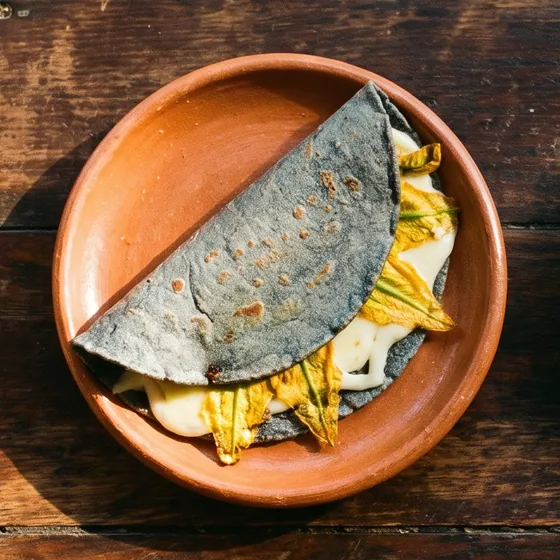 Quesadilla de masa azul con flor de calabaza y quesillo derretido, en plato de barro, vista desde arriba.