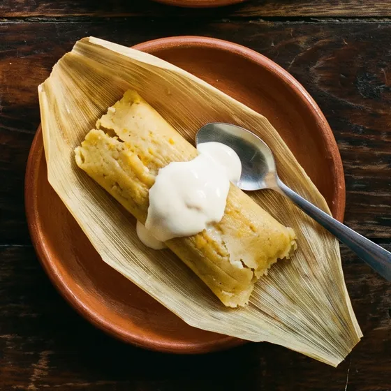 Tamal de elote abierto en su hoja, con una cucharada de nata.