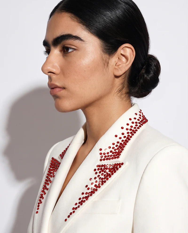 Perfil de la modelo con la solapa del saco Reforma bordada en cristal rojo, sobre papel blanco